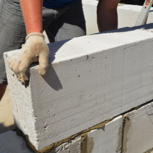 Gloved hands settling large concrete bricks onto mortar.