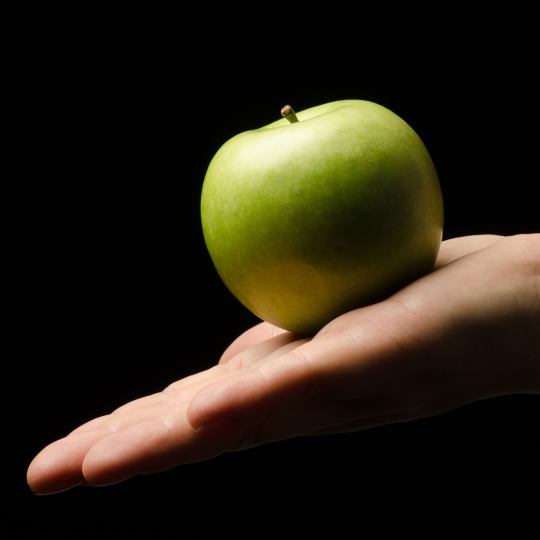 Image of a hand holding a green apple with a black background