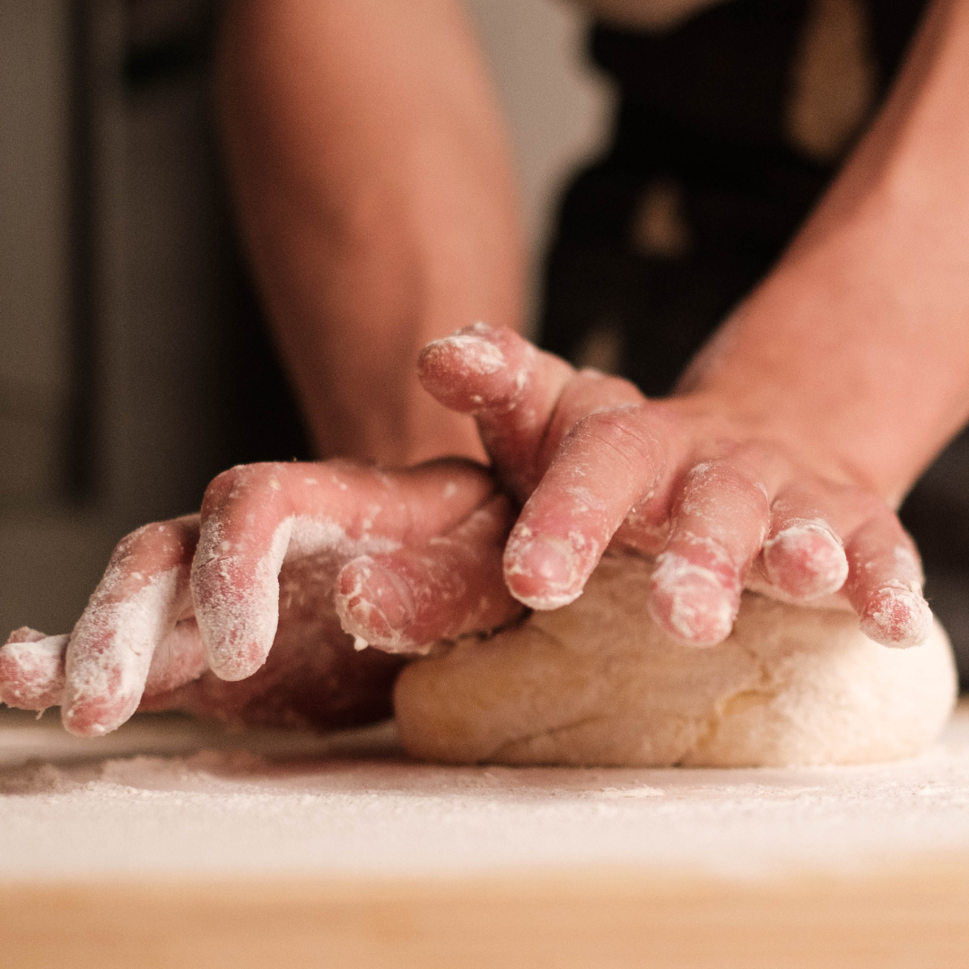 Image of two hand kneading a dough ball on a wooden cutting board. 