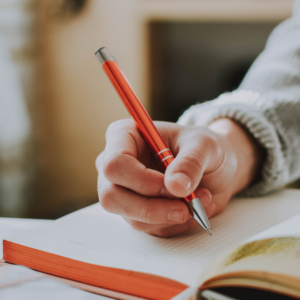 Close up of a hand writing in notebook with red pen. 